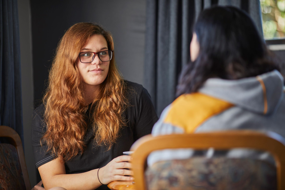 Two women engaged in a serious conversation at a table, discussing how to talk with someone experiencing family violence