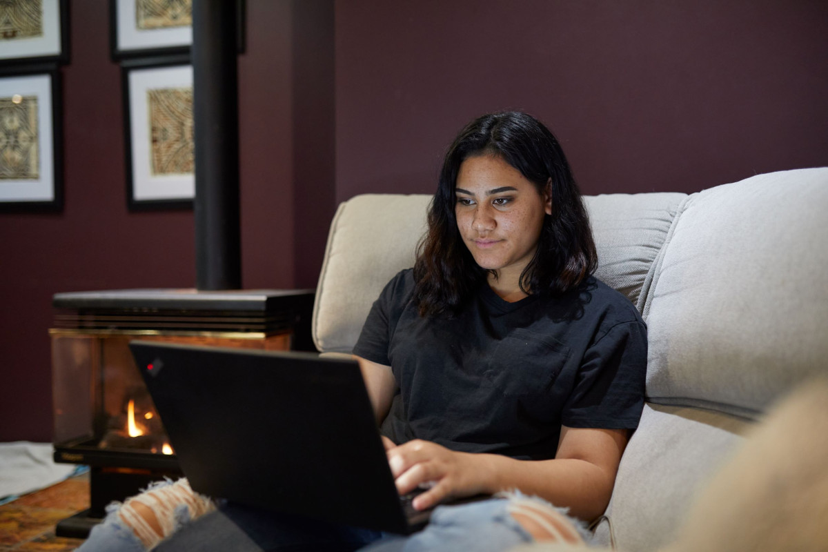 Young woman working on a laptop in a cosy living room, seeking online support for family violence issues