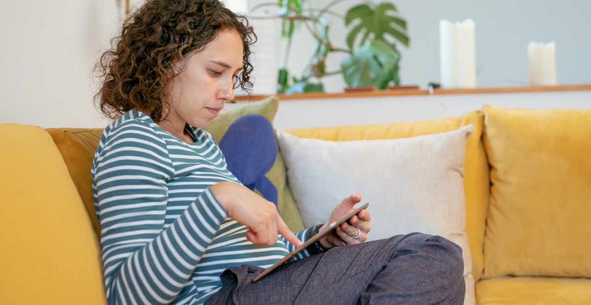 Woman sitting on a couch deeply engrossed in researching on a tablet, learning about unsafe relationships