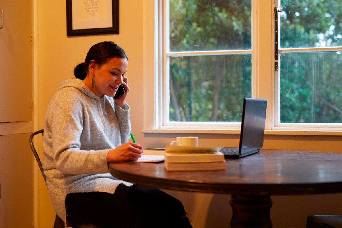 Woman smiling while talking on the phone and writing notes, representing accessible family violence services in New Zealand
